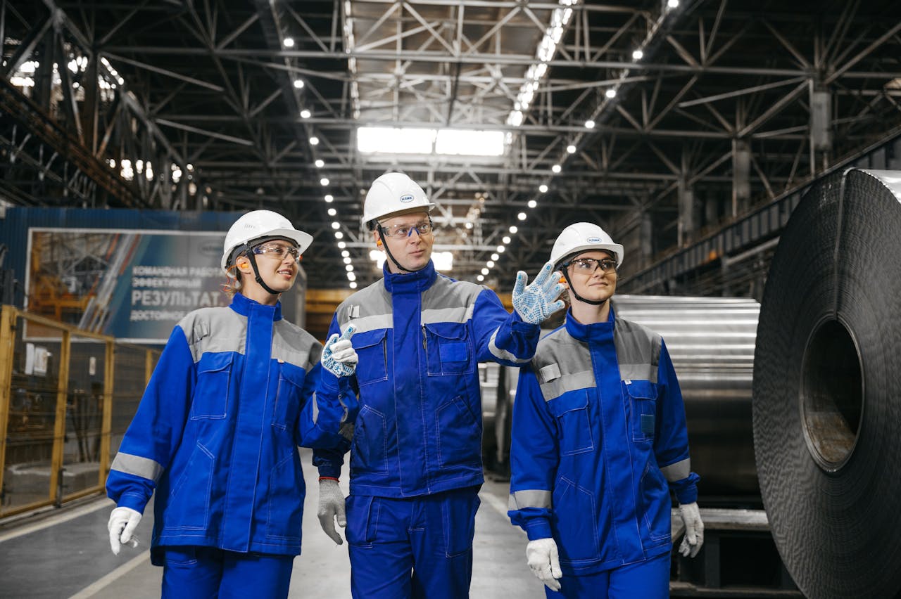 Group of workers in safety gear inside an industrial steel factory, engaging in discussion.